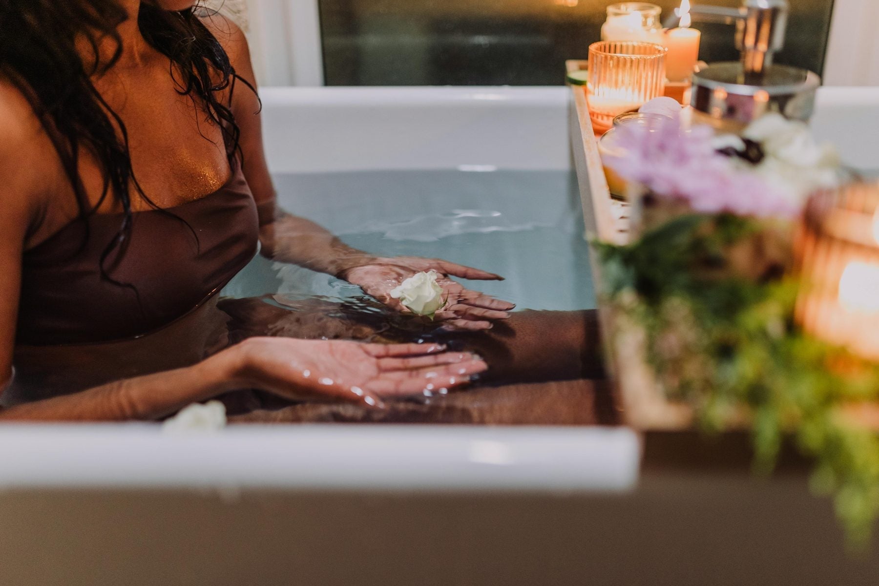 Woman relaxing in a ritual detox bath with candles and botanicals